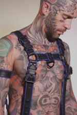 Model wearing a black and blue leather combat harness and connector with black metal hardware