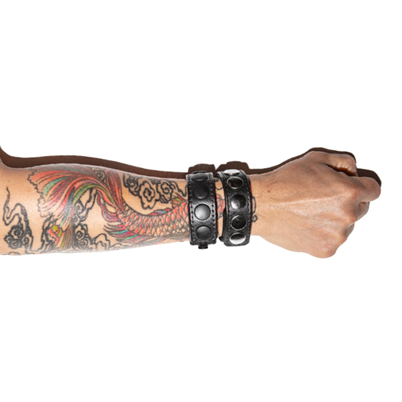 A pair of leather cockrings being worn on a tattooed forearm