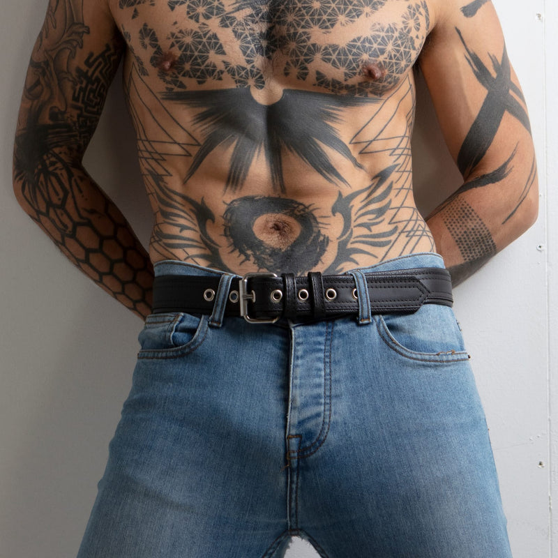 Front view of a tattooed model wearing jeans with a black leather belt with silver buckle