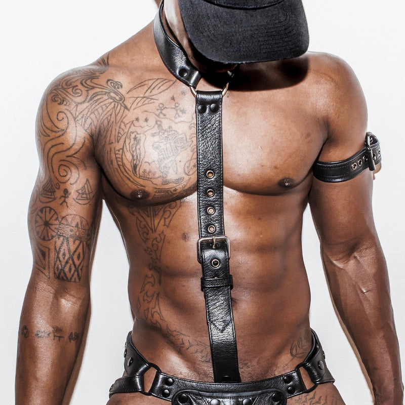 Black leather collar with cockstrap and black leather jockstrap being worn by a dark tattooed male model