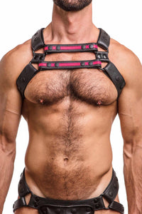 A hairy model wearing a UNIVERSAL X HARNESS - Fluro Pink with black rivets, snaps, and D-rings. Front straps parallel.