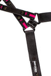 Flat-laid and facing down, a black and fluro pink leather harness with black rivets, snaps, and D-rings showing the lining.