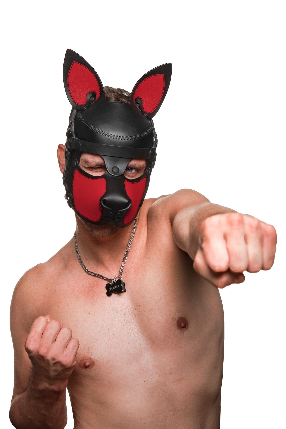 Framed from the chest up, a model in an Australian made leather pup hood with red snout and ears, punching straight forward.