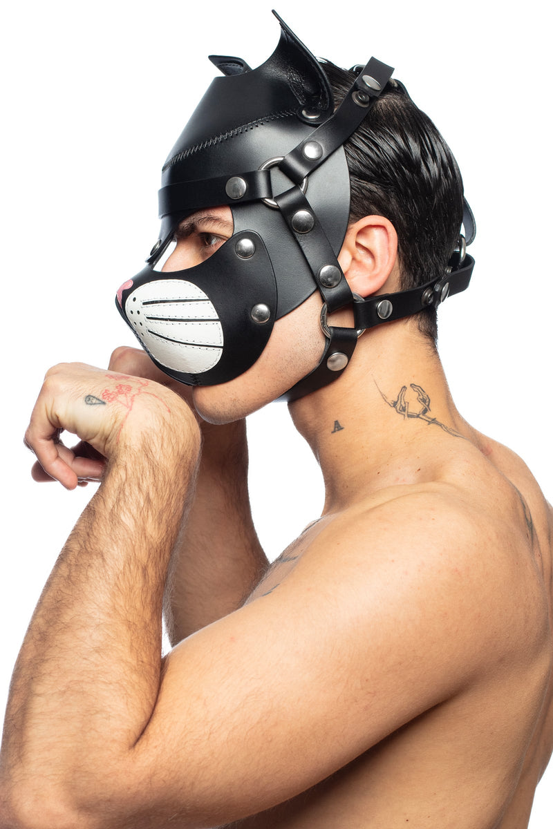 Side view of a man wearing a black and white leather cat hood, with stainless steel detailing, pretending to lick his paw.