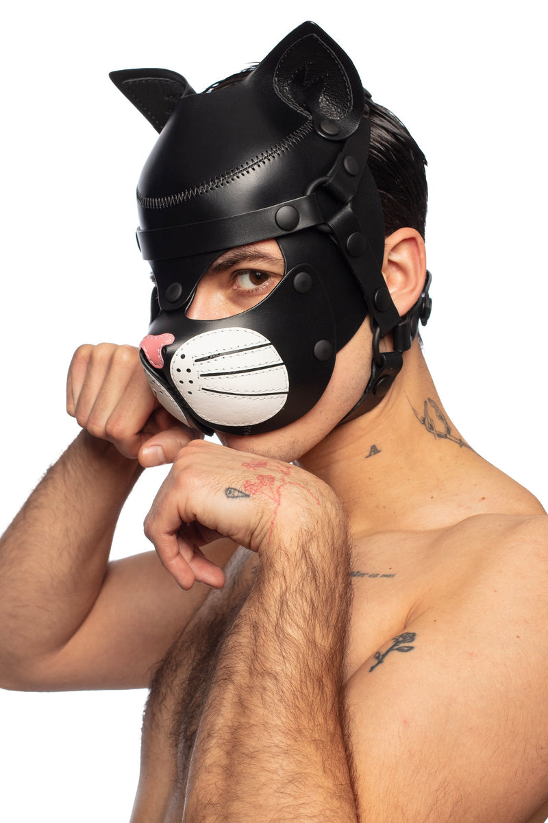 Playful model, striking a three-quarter pose, in an all leather black ARMY OF MEN TOMCAT hood, with white whisker pads.