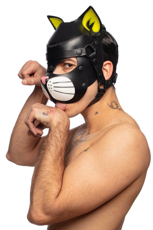 Captured from the side view, a model in a cat hood with fluro yellow ears pretends to lick his paw while looking at you.