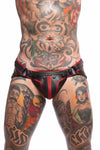 A striking model wearing a black and red leather Combat jock with matte black rivets, snaps, and O-rings, front facing view.