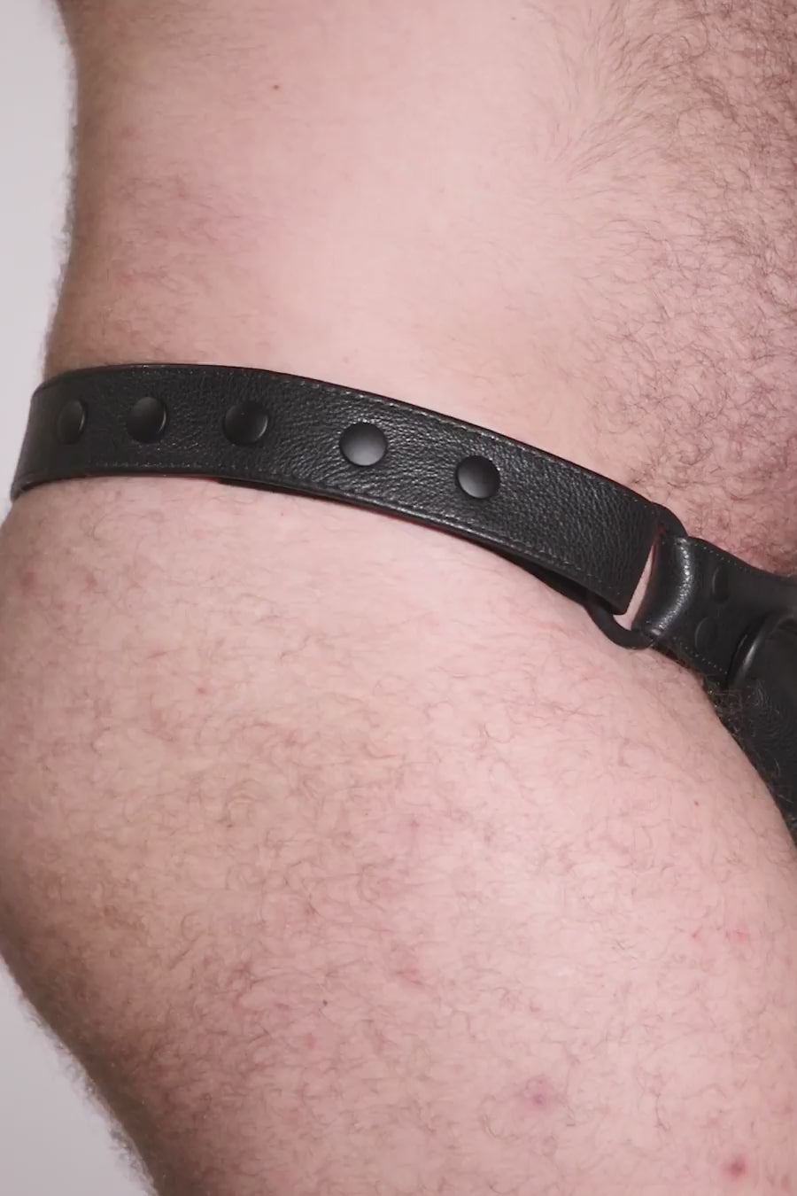 Video of a model wearing a black leather thong with a black harness codpiece. Matt black hardware