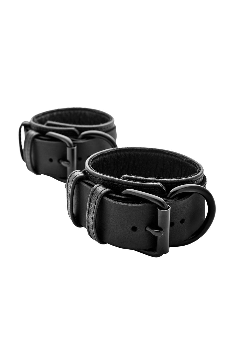 A pair of 2.25" wide ARMY OF MEN black leather restraints, coiled to display matte black hardware.