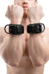 Front-on shot of male model wearing a pair of black and army green leather wrist restraints with matte black metal hardware.
