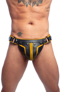 A tattooed model facing forward in an unique ARMY OF MEN COMBAT THONG - Yellow with matte black rivets, snaps, and O-rings.