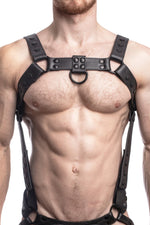 Model wearing a black leather bulldog harness and connector with black hardware. Connector attached to a jockstrap. Front.