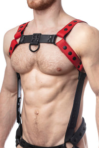 Model wearing a red leather bulldog harness and connector with black hardware. Connector attached to a jockstrap. Side.