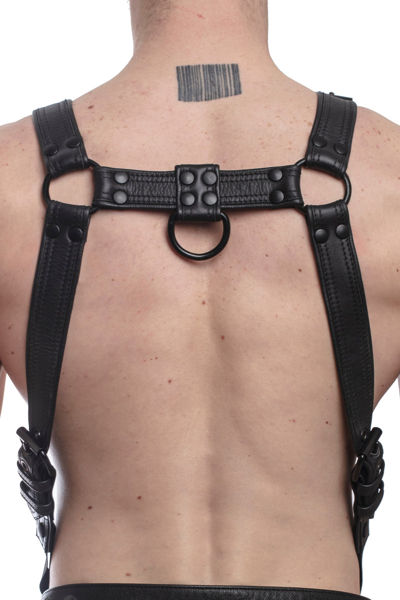 Model wearing a black leather combat harness and connector with black metal hardware. Back view.