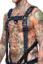 Model wearing a black and blue leather combat harness and connector with black metal hardware. Side view.