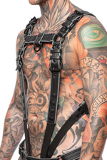 Model wearing a black and grey leather combat harness and connector with black metal hardware. Side view.