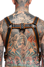 Model wearing a black and orange leather combat harness and connector with black metal hardware. Back view.