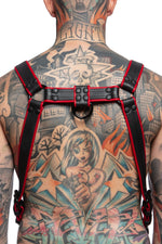 Model wearing a black and red leather combat harness and connector with black metal hardware. Back view.