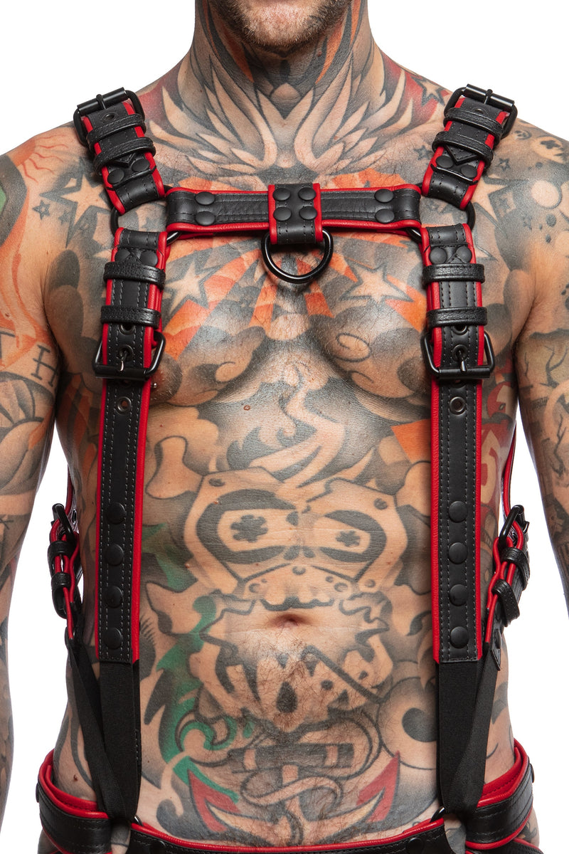 Model wearing a black and red leather combat harness and connector with black metal hardware. Front view.