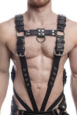 Model wearing a black leather combat harness and connector with stainless steel hardware, connected to a cockring. Front view.