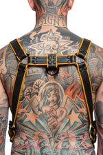 Model wearing a black and yellow leather combat harness and connector with black metal hardware. Back view.