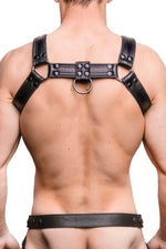 Model wearing a black leather combat harness with black metal hardware. Back view.