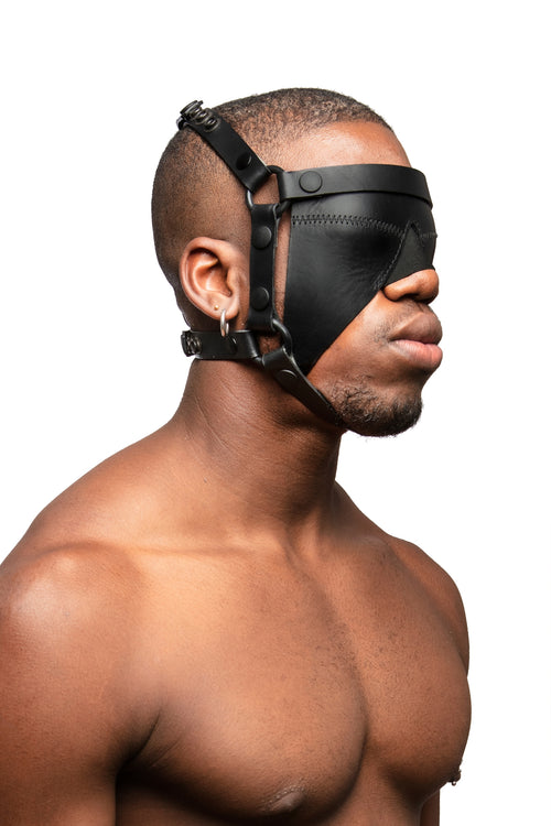Model wearing black leather head harness and blinder with black metal hardware. Three quarter view.