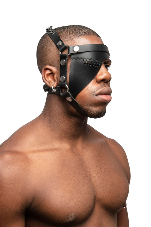 Model wearing black leather head harness and eye patch with stainless steel hardware. Three quarter view.