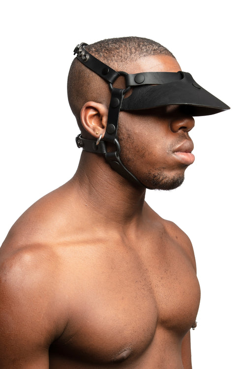 Model wearing black leather head harness and visor with black metal hardware. 